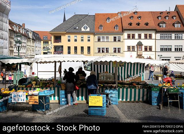 15 April 2020, Thuringia, Weimar: People buy at the market, a sign points out the rules of distance. Because of the effects and regulations surrounding the...