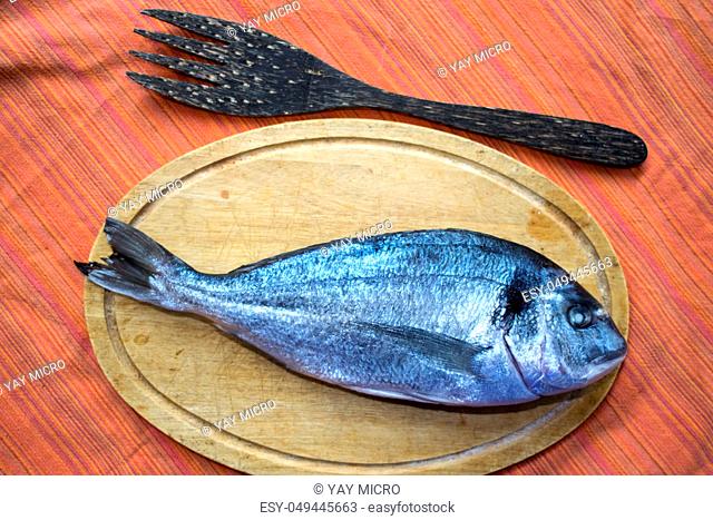 fresh gilthead sea bream fish on wooden dish with near fork and knife