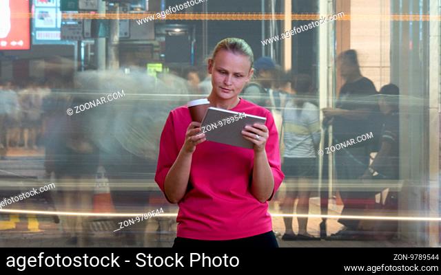 Young woman with coffee and tablet computer standing in busy crowded streets of Hong Kong