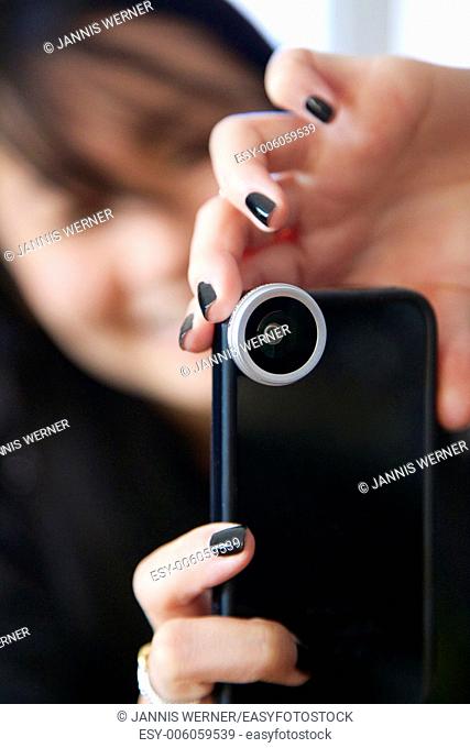 Girl takes a photo with her smartphone with a large smartphone lens attached