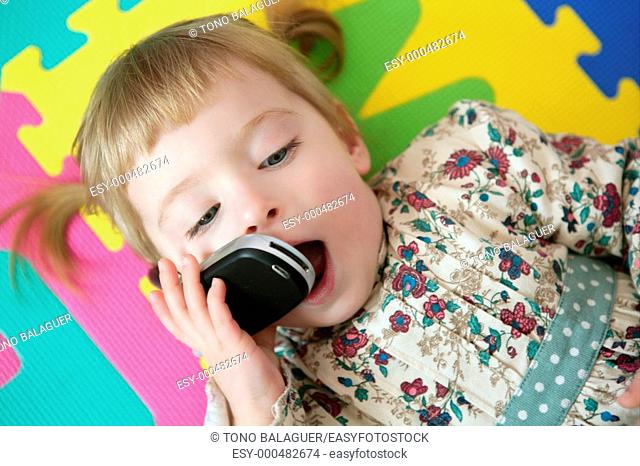 Funny toddler blond girl talking with mobile cell phone
