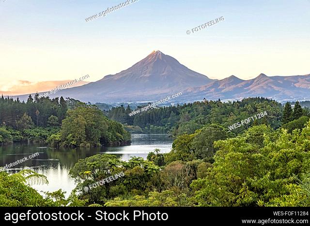 New Zealand, Scenic view of green forest surrounding Lake Mangamahoe with Mount Taranaki looming in background