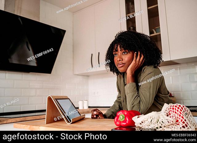 Thoughtful woman leaning on kitchen island at home