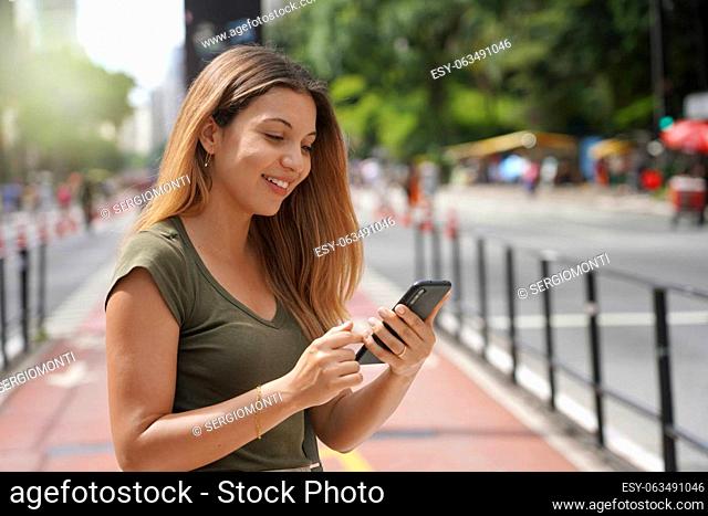 Smiling beautiful girl on Paulista Avenue using smartphone, Sao Paulo, Brazil