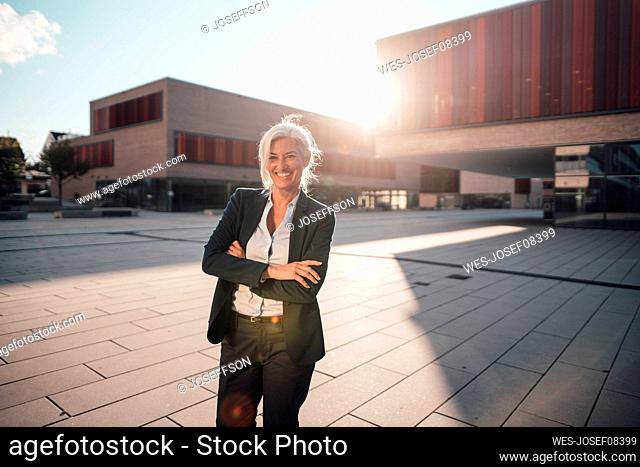Happy businesswoman standing with arms crossed at office park on sunny day