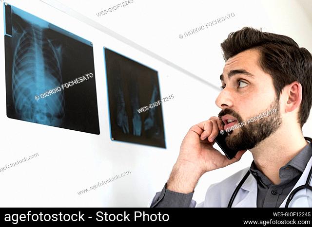 Male doctor looking at X-ray while talking on mobile phone