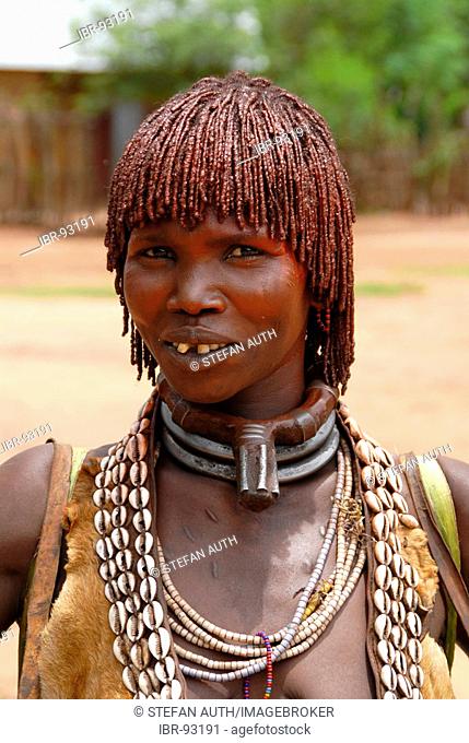 Portrait woman of the Hamar people wears a leather cloth and typical clay hairdo a metal and kauri mussel chain at the market of Dimeka Ethiopia
