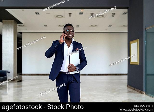 Young businessman walking while talking on smart phone with laptop