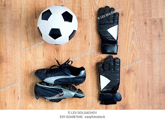 sport, soccer, football and sports equipment concept - close up of ball, boots and goalkeeper gloves on wooden background