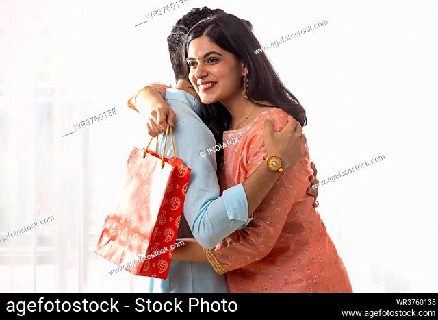 A HAPPY YOUNG WOMAN EMBRACING BROTHER WHILE HOLDING GIFT