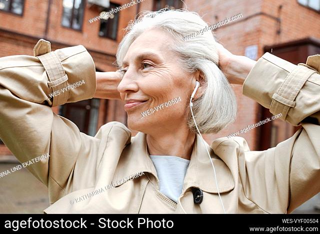 Mature woman with hands behind head listening music through headphones