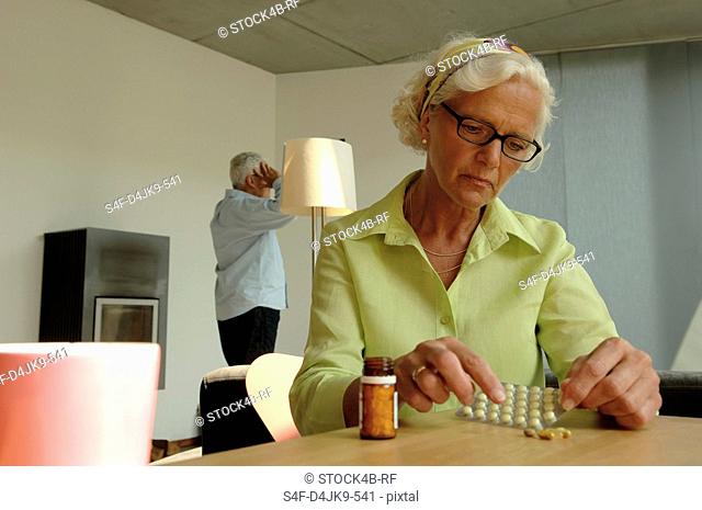Senior woman holding a glass with pharmaceuticals in one hand while looking unhappy, close-up