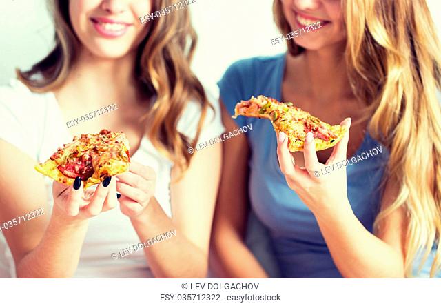 friendship, people, pajama party and junk food concept - close up of happy friends or teenage girls eating pizza at home