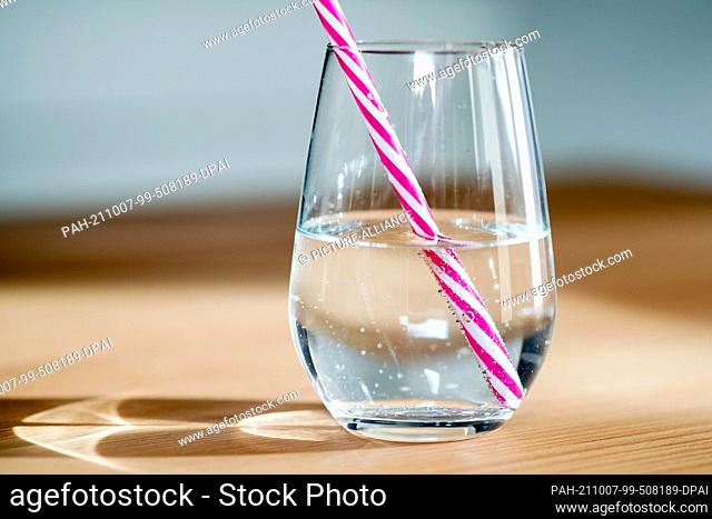 ILLUSTRATION - 01 October 2021, Lower Saxony, Oldenburg: A glass of water with a reusable drinking straw made of hard plastic stands on a table