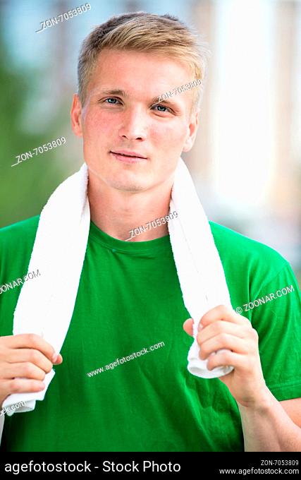 Tired man with white towel after fitness time and exercising in city street park at beautiful summer day. Sporty model caucasian ethnicity training outdoor