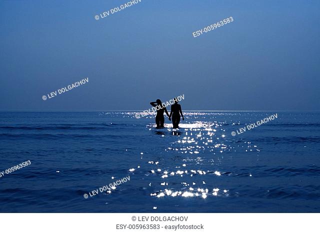 silhouette of two girls holding hands in the sea