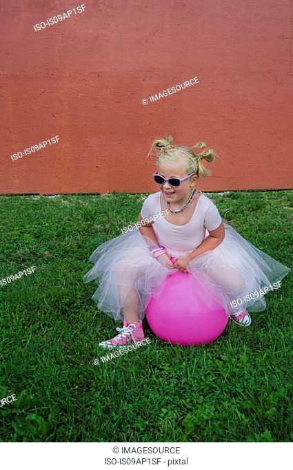 Young girl wearing tutu, bouncing on pink inflatable hopper