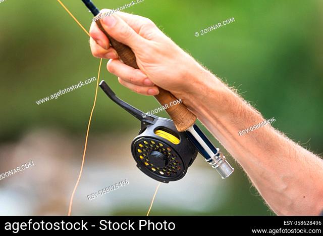 Man fly fishing with reel and rod. Sport fly fisher man close up on reel