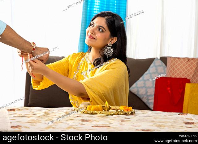 A HAPPY YOUNG WOMAN LOOKING ABOVE AND TYING RAKHI