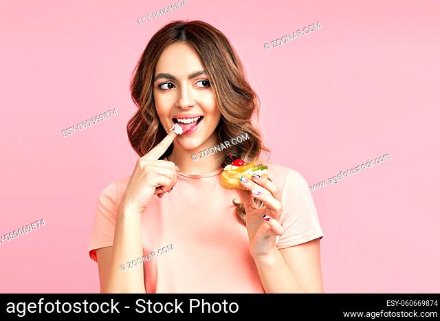 Smiling pretty female eating delicious pastry cake on pink background. Food, sweets concept