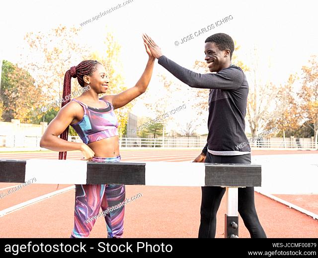 Male and female athlete giving high-five while standing by beam on running track