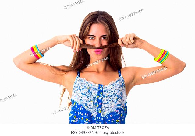 Young pretty woman in blue and white T-shirt with colored bracelets making moustache of her long brown hair on white background in studio