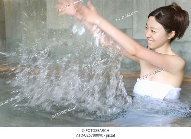Woman splashing water in hot tub, smiling, side view, blurred motion, Japan