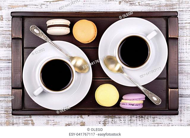 Two cups of coffee, spoon and macaron cakes on tray on white wooden table. Lifestyle concept. Close up. Top view