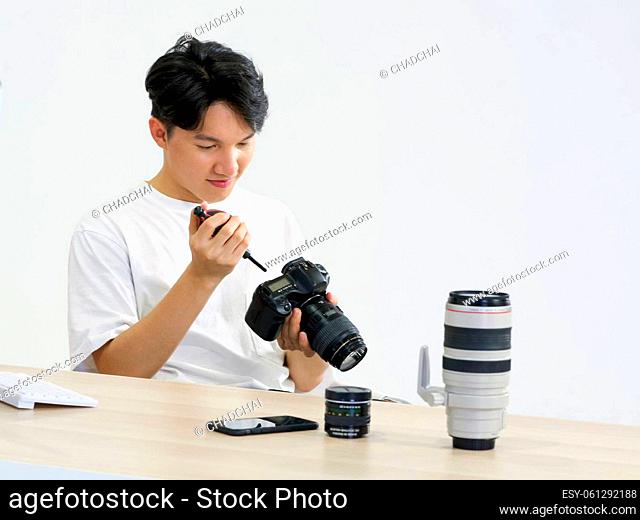 Young asian photographer is cleaning the camera screen and body with a blower camera for cleaning on his desk