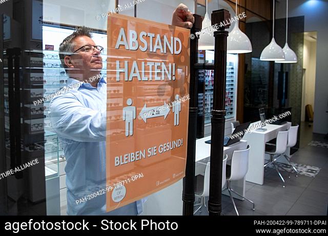 22 April 2020, Berlin: An optician hangs a sign in his shop in the Mall of Berlin with the inscription ""Keep your distance! - Stay healthy!"" on the front door