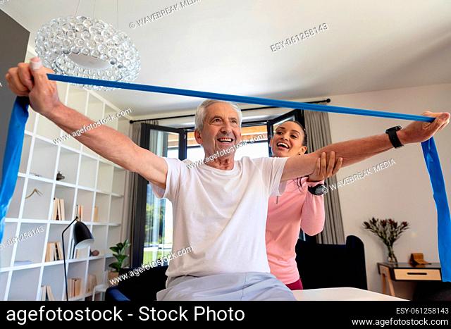 Biracial female physiotherapist assisting happy caucasian senior man stretching resistance band