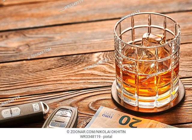 Glass of whiskey or alcohol drink with ice cubes and car key on rustic wooden table with copy-space. Drink and drive and alcoholism concept