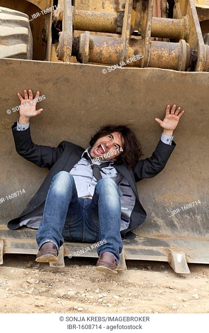 Young man lying in the bucket of an excavator screaming