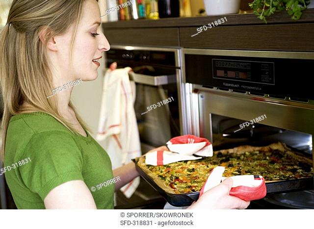 Young woman putting vegetable pizza into oven on baking tray