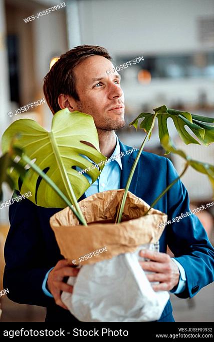 Smiling mature businessman with Monstera plant in sack at cafe