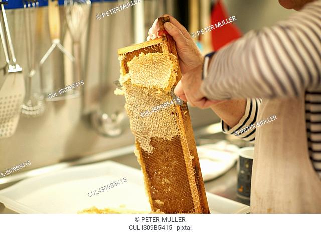 Cropped image of female beekeeper scraping honeycomb in kitchen