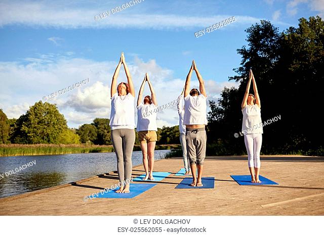 fitness, sport, yoga and healthy lifestyle concept - group of people making upward salute pose on river or lake berth