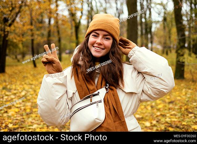Happy young woman peace gesturing in autumn park