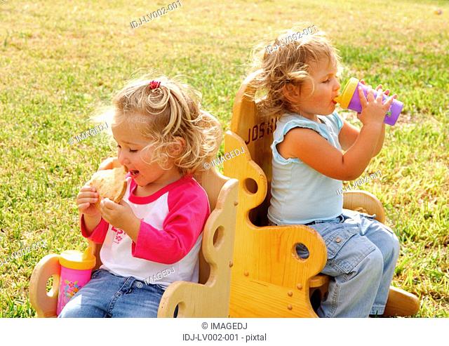 Close-up of a girl eating a slice of bread and her sister drinking water from a bottle
