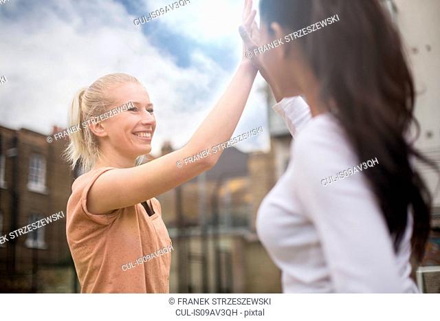 Two young women giving high five, outdoors