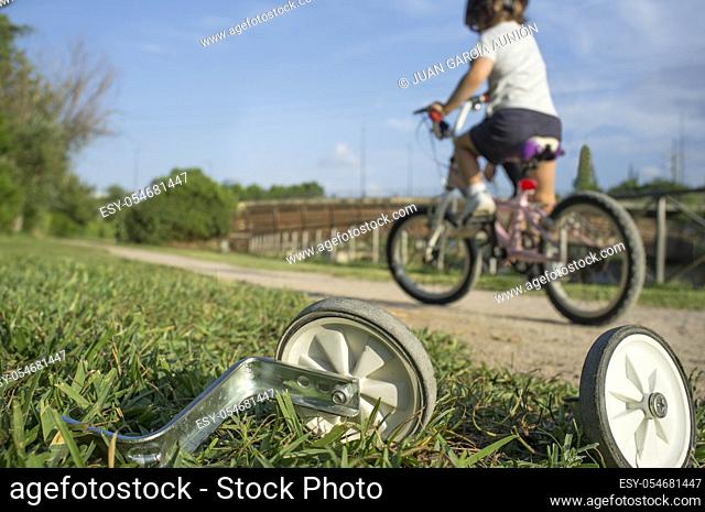 Additional wheels lying on the grass while a boy begins to ride without them. First day without training wheels concept
