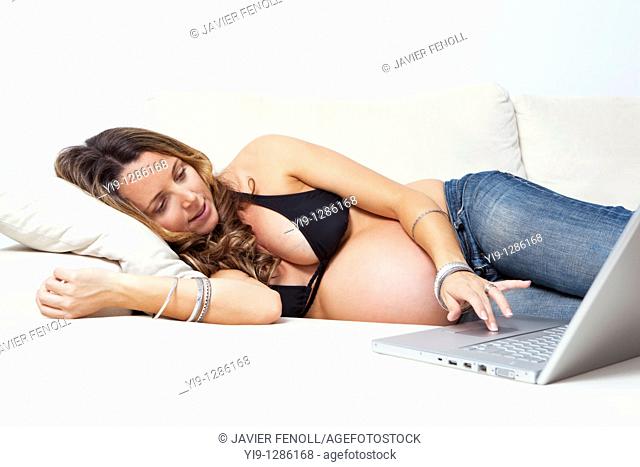 Portrait of a pregnant woman lying on a couch with a laptop in front of her