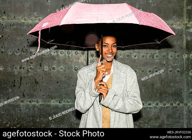Teenage girl with umbrella standing in front of black wall