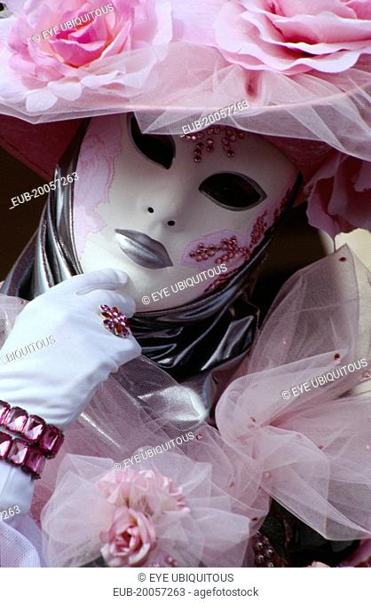Venice Carnevale. Close up portrait of a female figure dressed in a white and pink floral costume and mask