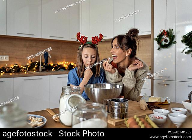 Happy woman with daughter tasting cookie frosting in kitchen