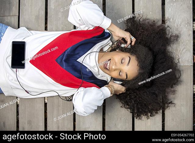 From above shot of relaxed happy woman wearing headset and singing while lying and having fun on wood