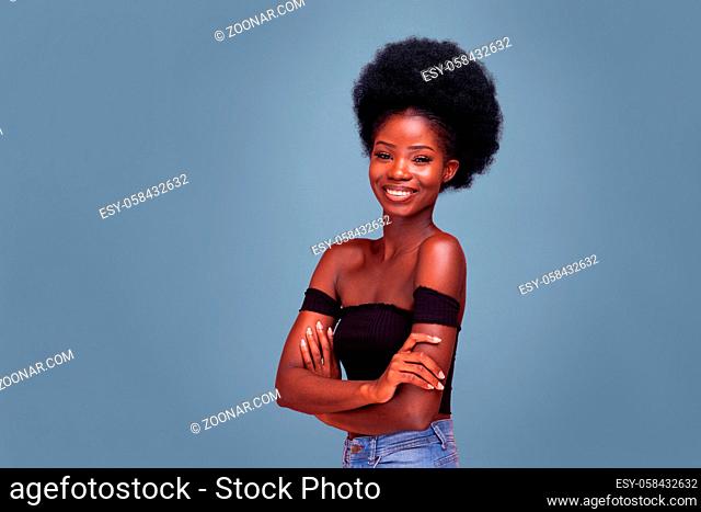 Smiling Confident young African American girl with afro hair standing with arms folded in black bare shoulder top and blue denim jeans