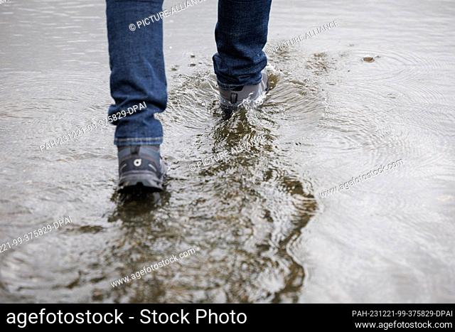 21 December 2023, Lower Saxony, Osnabrück: A walker crosses the part of a footpath that has been flooded by the rain. The German Weather Service is expecting...