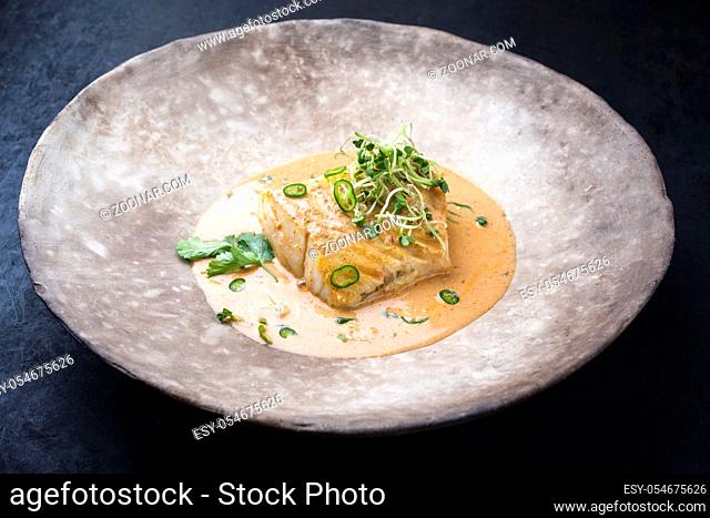 Gourmet fried skrei cod fish in Thai curry with chili and sprouts as closeup on a modern design plate with copy space