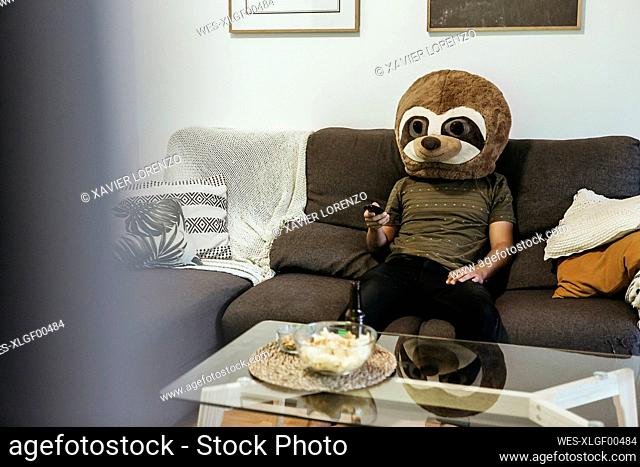 Mid adult man wearing teddy bear mask watching TV while sitting in living room